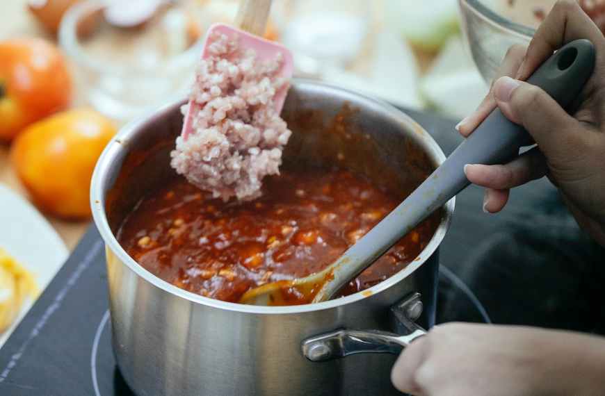 crop person cooking chili with meat in kitchen